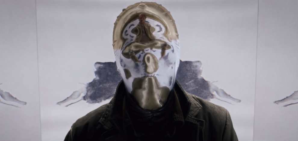 Clicca per vedere l'immagine originale Looking Glass indossa un cappotto nero e una maschera argentata
