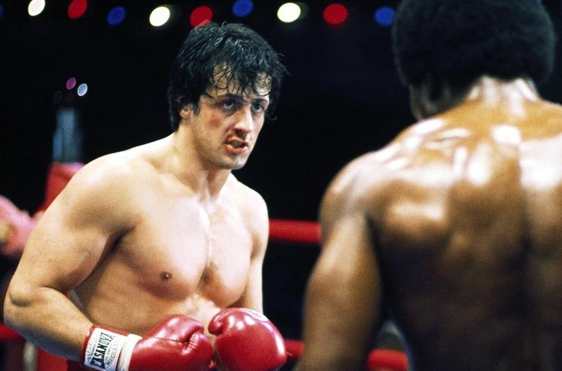 Un'immagine che vede Sylvester Stallone nei panni di Rocky Balboa mentre bonxa con Apollo Creed in Rocky