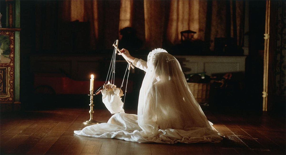 Una bambina coperta da un velo bianco gioca con una marionetta al lume di candela