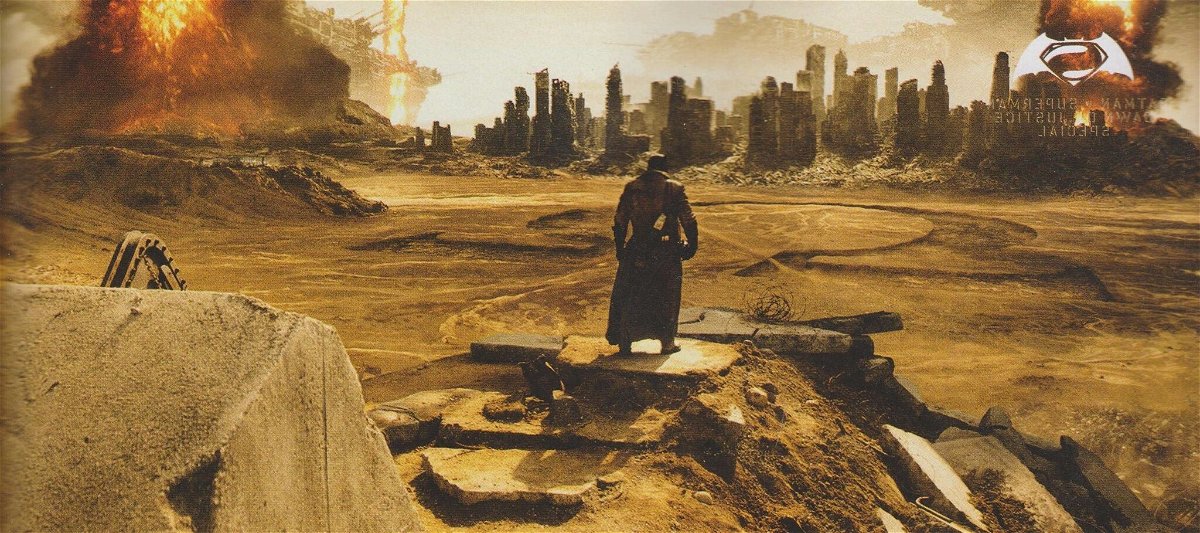 Vista panoramica di Batman di fronte a una città distrutta e un'enorme omega disegnata sul terreno sabbioso