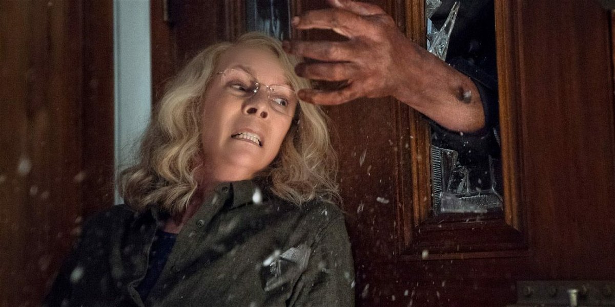 Jamie Lee Curtis nei panni di Laurie Strode in una scena del film Halloween, mentre viene afferrata dalla mano di Michael Myers che sfonda il vetro di una porta