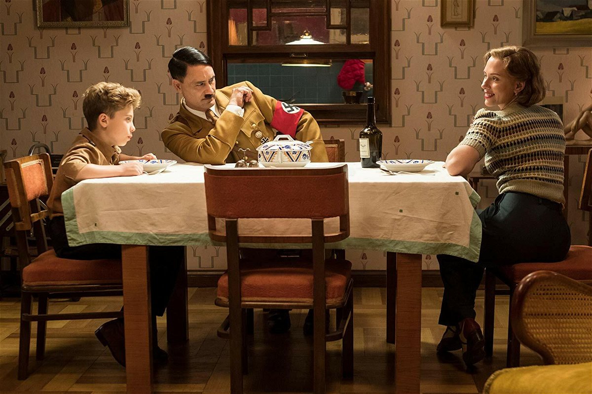 Roman Griffin Davis, Taika Waititi e Scarlett Johansson seduti al tavolo in una scena del film