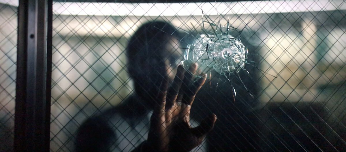 Il protagonista osserva un vetro incrinato da un foro di proiettile