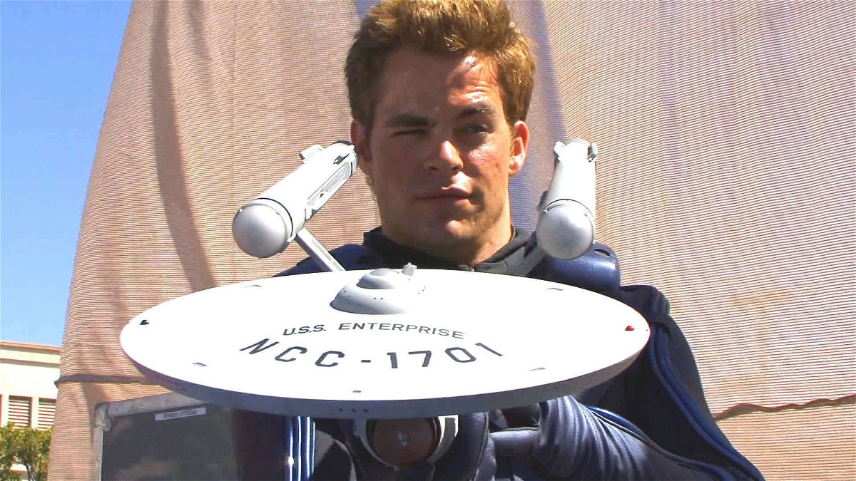 Chris Pine con un'espressione sorniona osserva il retro di un modellino dell'astronave U.S.S. Enterprise del Capitano Kirk