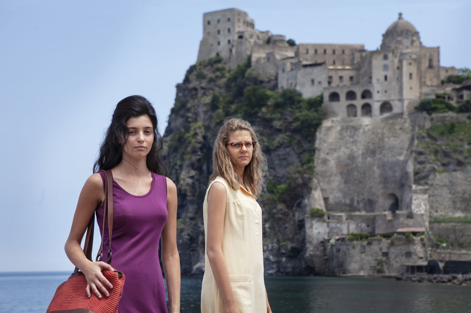 Clicca per vedere l'immagine originale Lila ed Elena guardano la telecamera, sullo sfondo il Castello Aragonese di Ischia